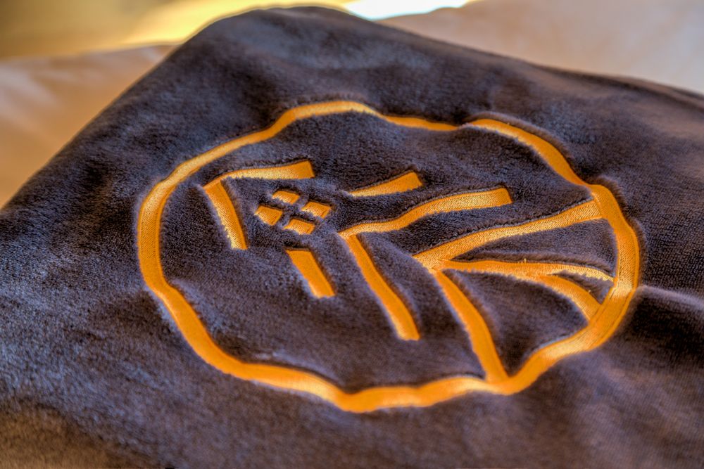 Nahaufnahme eines dunkelgrauen Stoffes mit orangefarbenem Hauslogo.