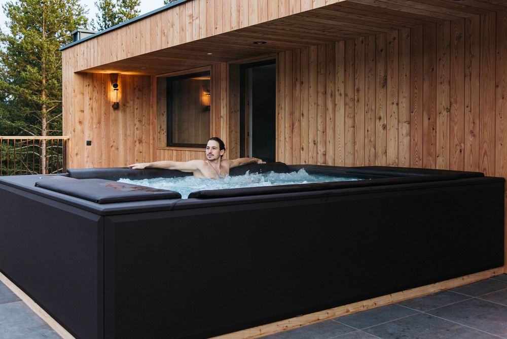 Mann entspannt im Whirlpool auf einer Terrasse mit Holzverkleidung.