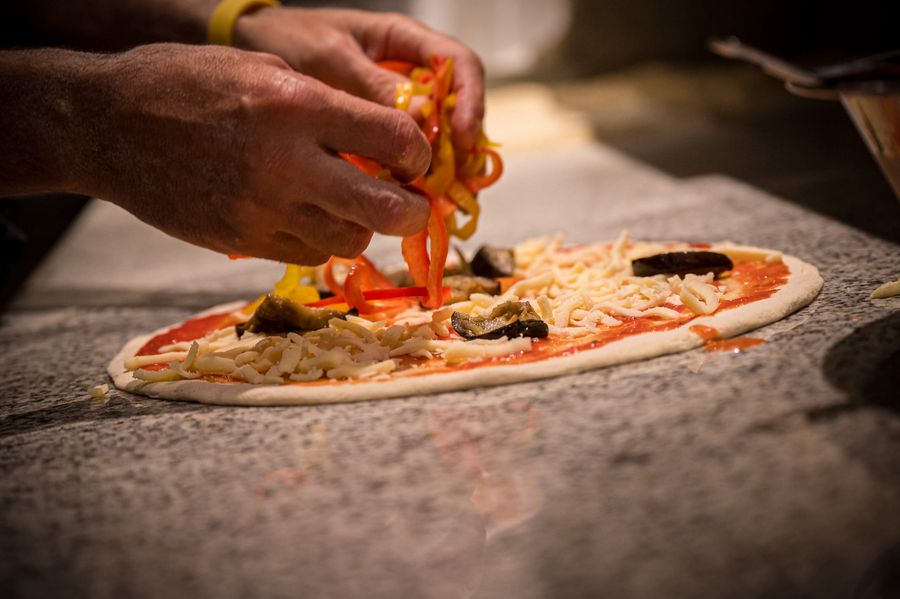 Hände belegen Pizza mit Paprika und Käse