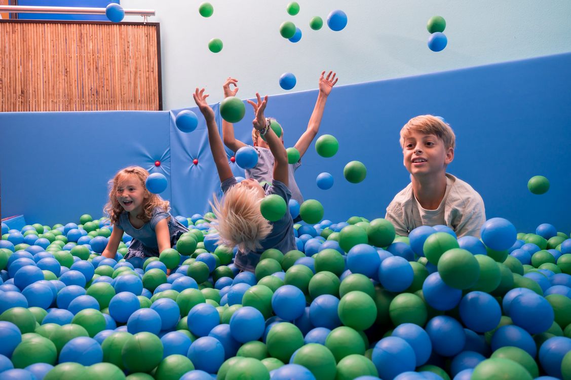 Kinder spielen fröhlich in einem Bällebad mit blauen und grünen Bällen
