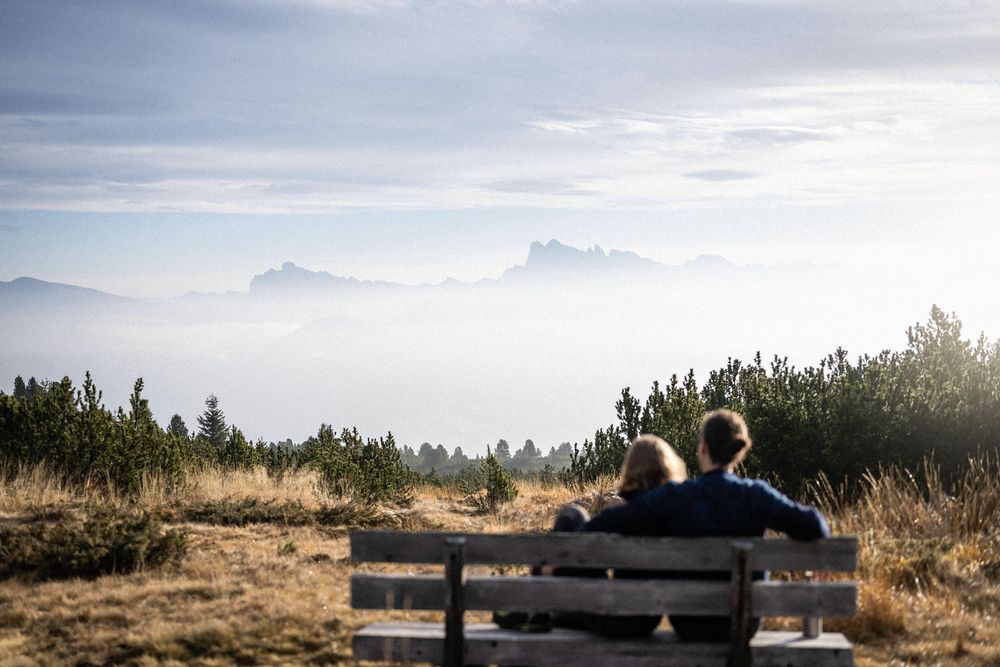 Ein Paar sitzt auf einer Bank und blickt auf nebelverhangene Berge.