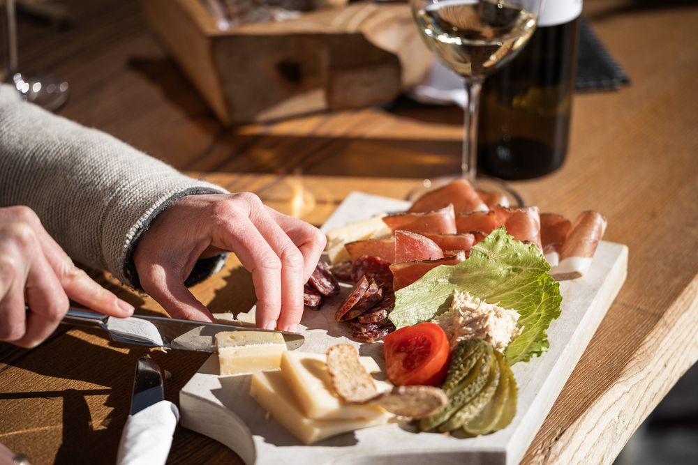 Taglio di formaggi e salumi su tagliere con vino bianco