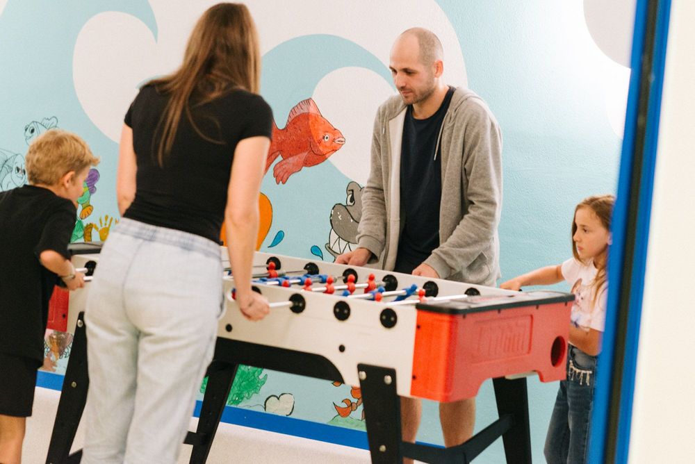 Zwei Erwachsene und zwei Kinder spielen Tischfußball vor einer Wand mit Meeresmotiven.