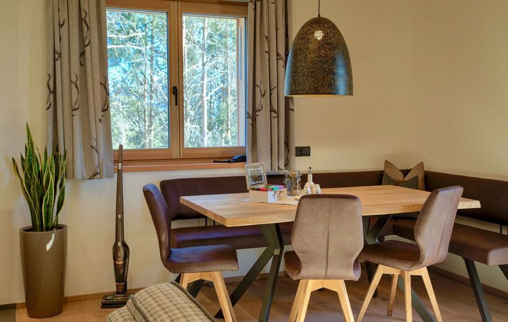 Gemütlicher Essbereich mit Holztisch, Stühlen, Eckbank und großen Fenstern mit Waldblick.