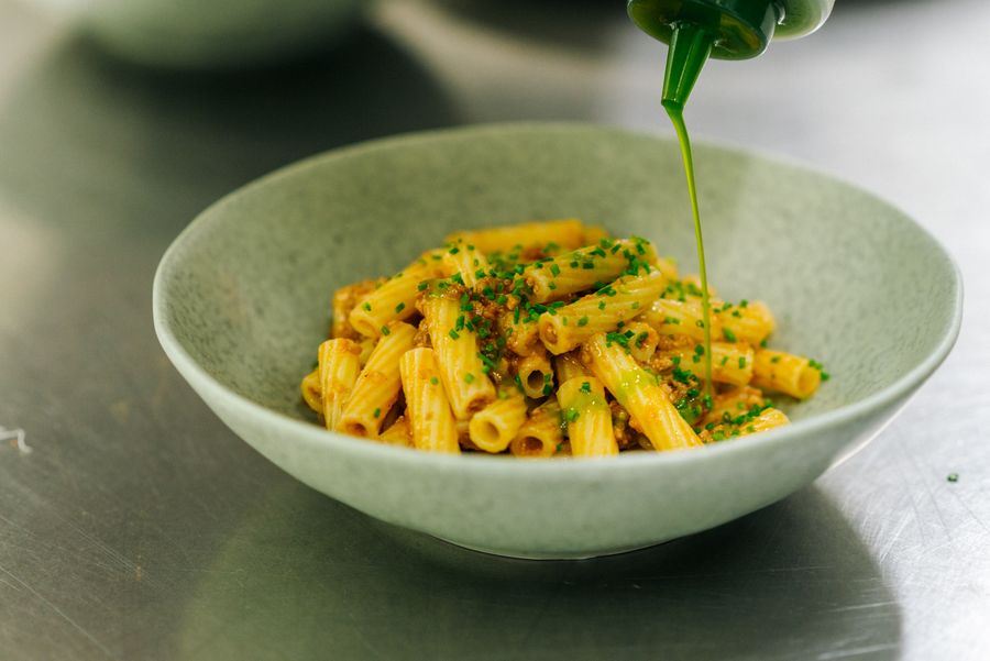 Teller mit Pasta, darüber wird grüne Sauce gegossen.