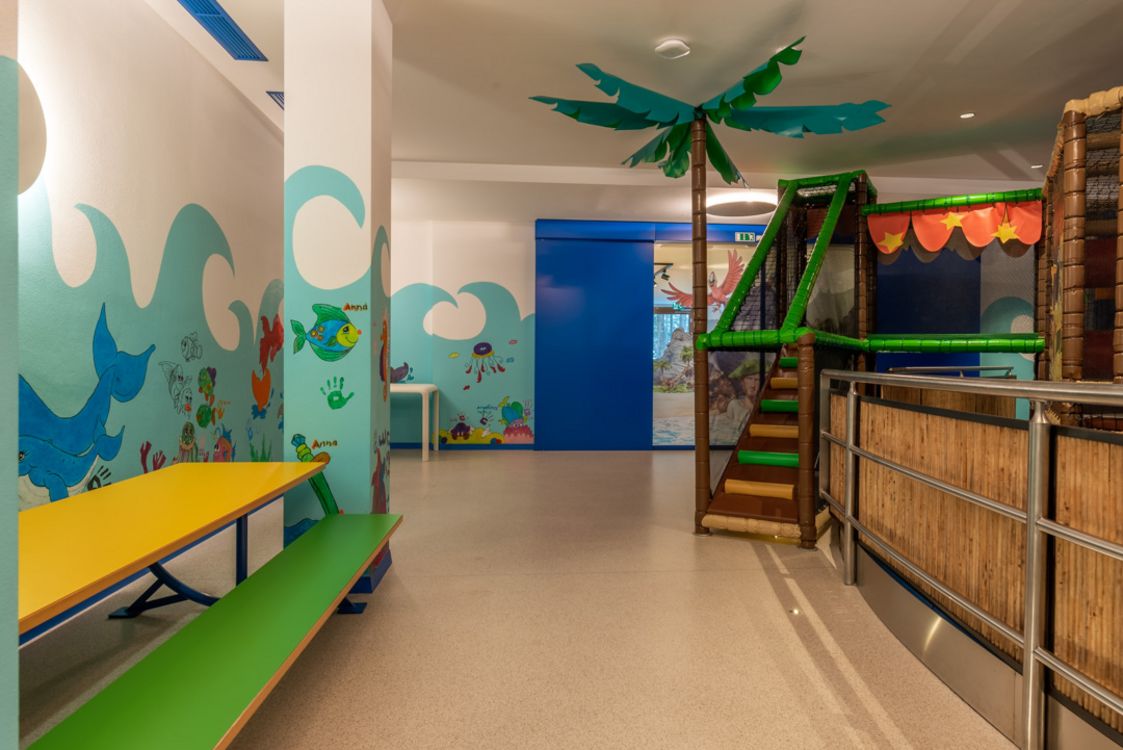 Bunter Kinderspielraum mit Wandmalereien und Spielgerüst mit Palme.