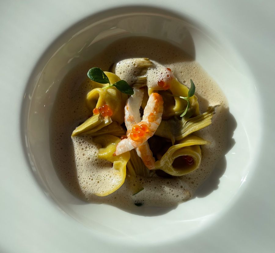 Feines Gericht mit Tortellini, Garnelen, Artischocken und Schaum auf weißem Teller