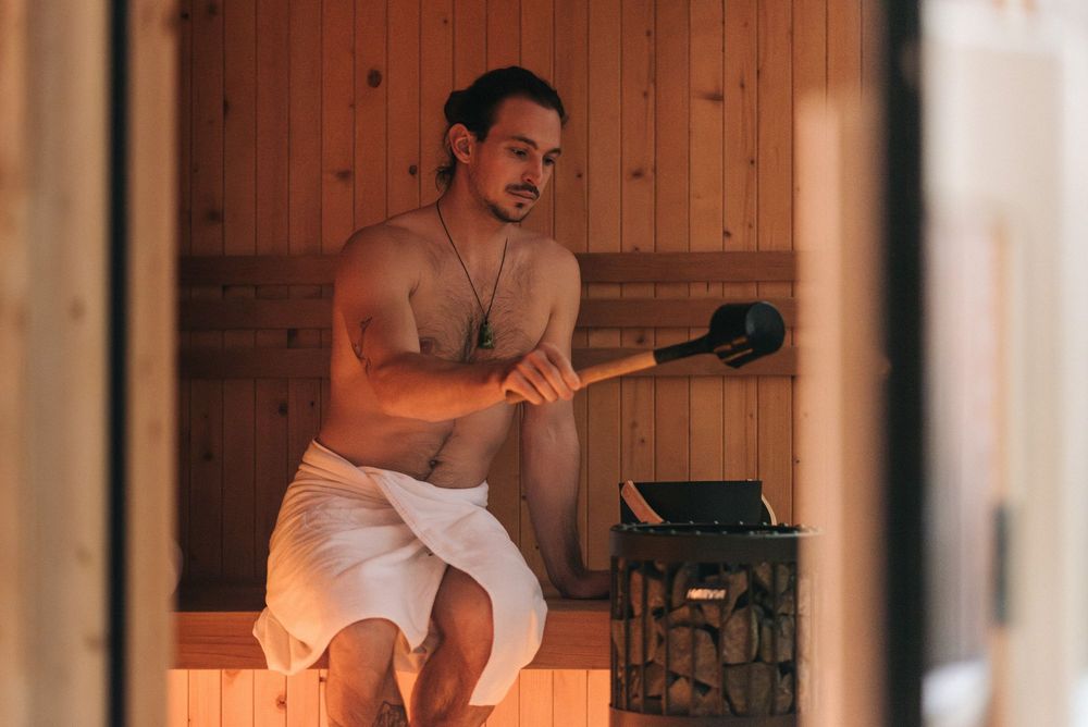 Uomo seduto in sauna con asciugamano bianco mentre tiene un mestolo per il vapore.