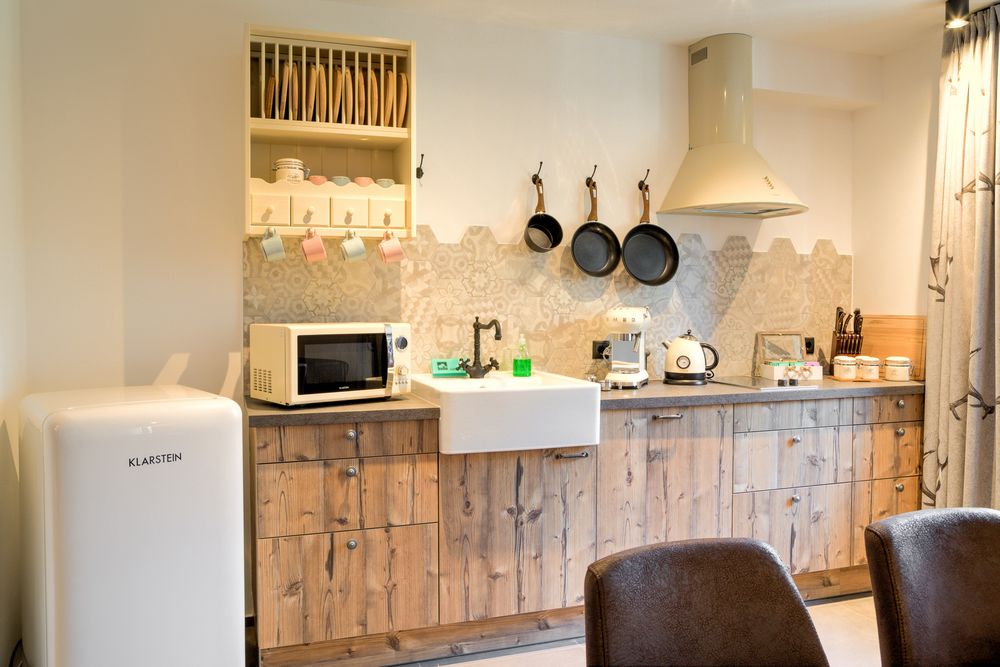 Kleine Küche mit Holzfronten, Kühlschrank, Mikrowelle, Waschbecken, Kaffeemaschine und Pfannen an der Wand.