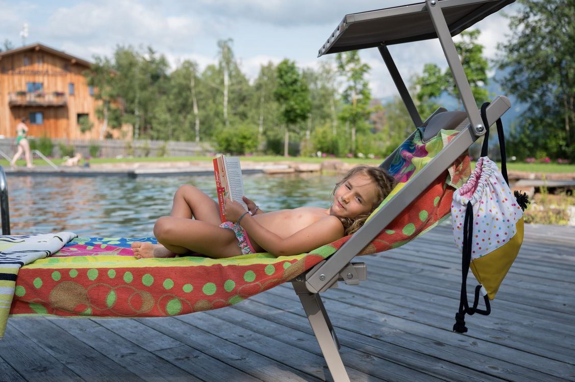 Kind liest buch auf liegestuhl neben pool im freien