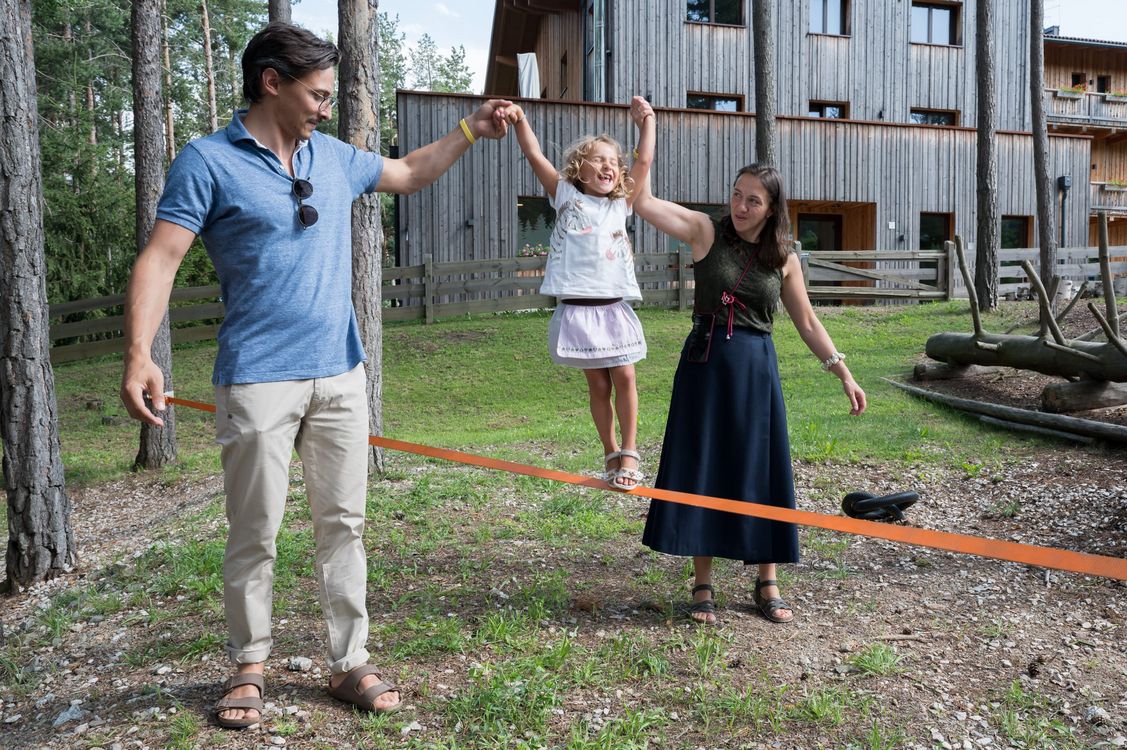 Kind wird von Eltern an Händen haltend auf einer Slackline gehalten.