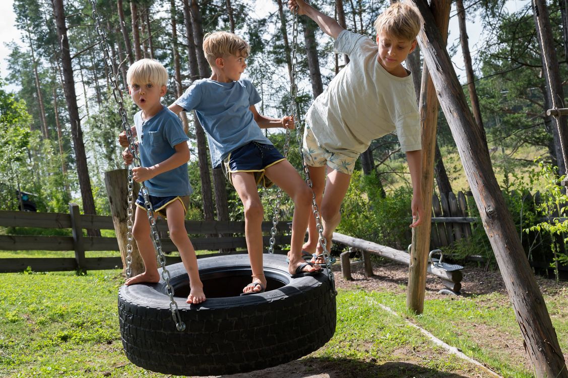 Drei Jungen spielen gemeinsam auf einer Reifenschaukel im Freien