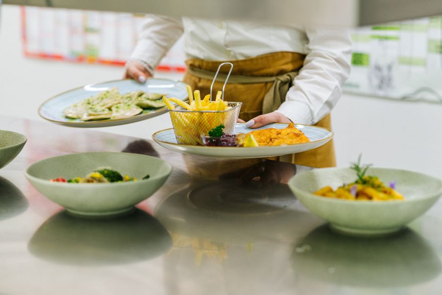 Kellner trägt Teller mit Pommes und Schnitzel sowie mit Ravioli.