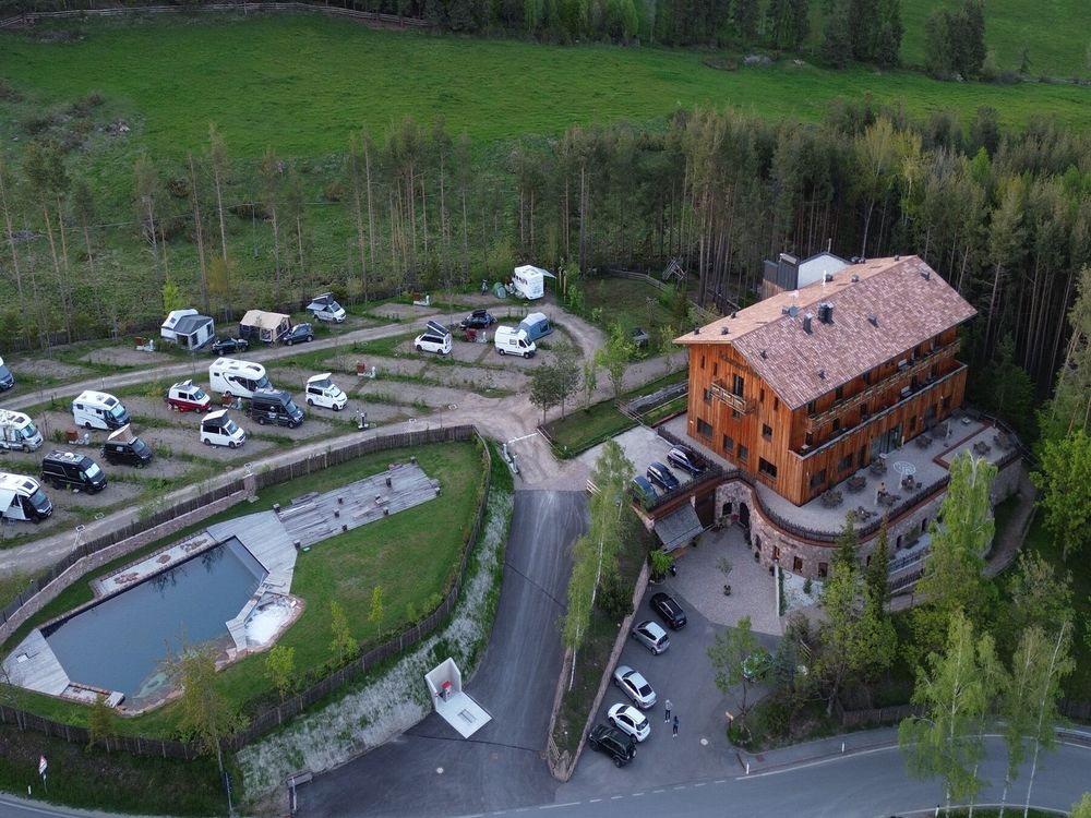 Vista aerea di un campeggio con roulotte, un edificio in legno e una piscina circondata da alberi.