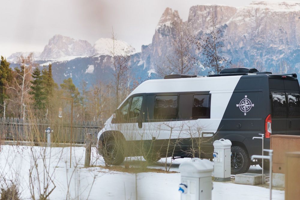 Camper parcheggiato in un paesaggio innevato con montagne sullo sfondo.