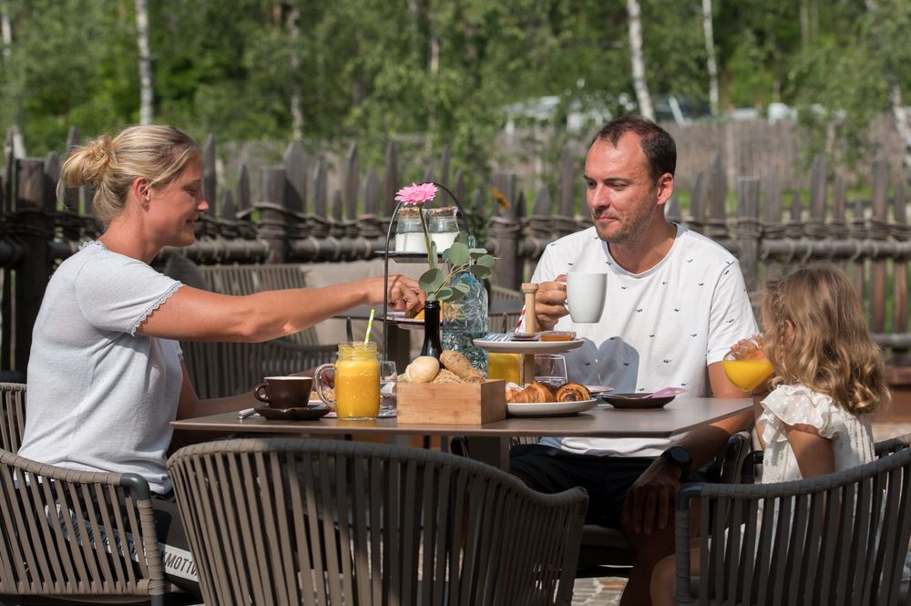 Familie beim Frühstück im Freien mit Getränken und Gebäck.
