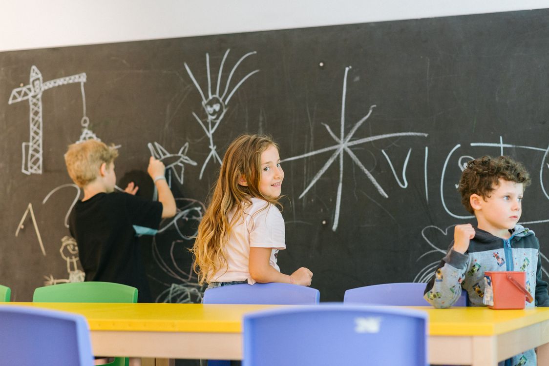 Kinder malen mit Kreide an einer Tafel im Klassenraum.