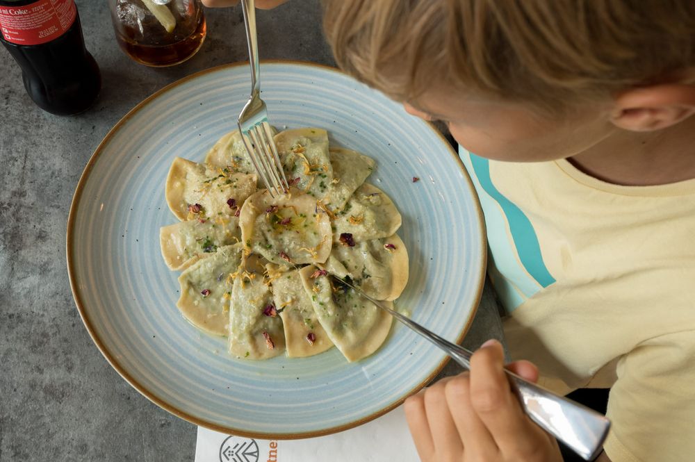 Kind isst Ravioli auf blauem Teller mit einem Glas Cola und einer Flasche neben dem Teller