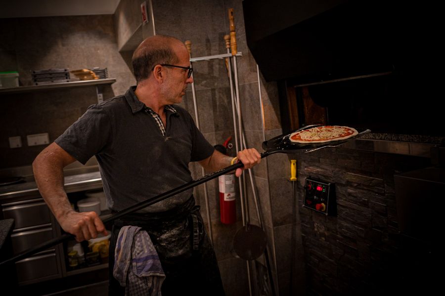 Mann schiebt Pizza mit langem Schieber in Steinofen