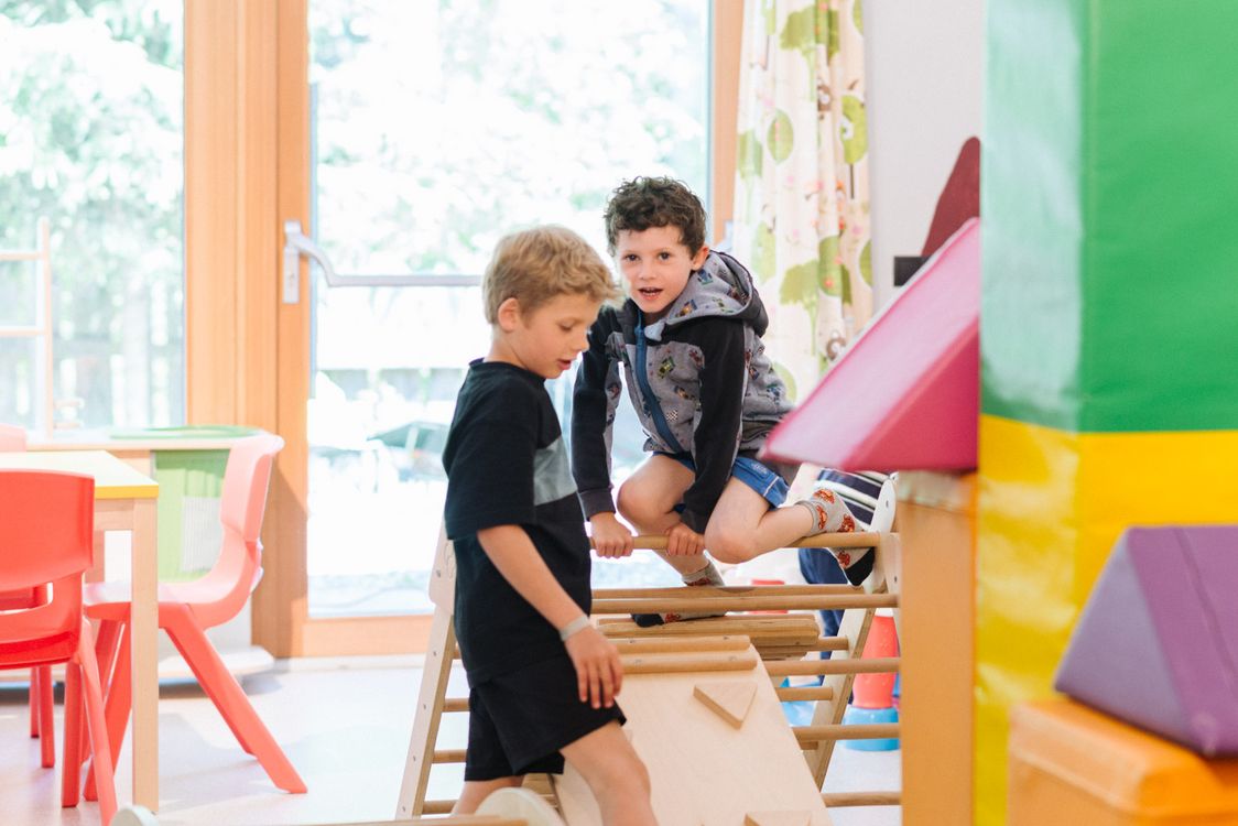 Zwei Jungen spielen in einem hellen Innenraum mit Klettergeräten und bunten Möbeln.