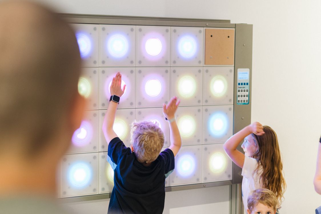 Kinder spielen an einem beleuchteten interaktiven Wandspiel.