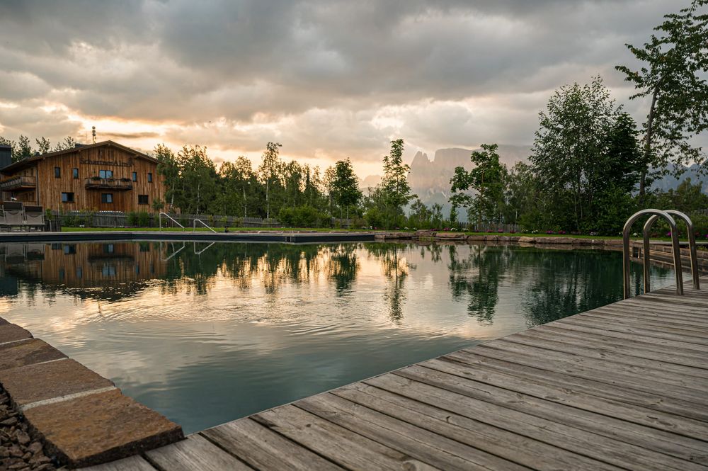Schwimmteich mit Holzsteg und Alpenhütte bei Sonnenuntergang