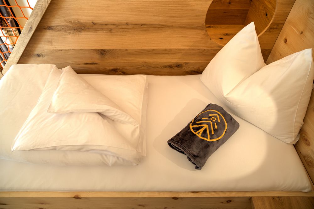 Gemachtes Bett mit weißer Bettwäsche und einem grauen Handtuch mit Stickerei auf einem Holzrahmen.