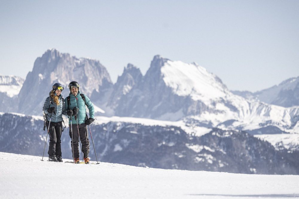 Zwei Skifahrer stehen im Schnee vor schneebedeckten Bergen.