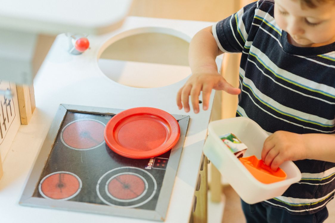 Kind spielt mit Spielküche und rotem Teller