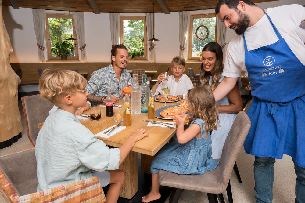Familie sitzt an einem Tisch im Restaurant, Kellner serviert Pizza.