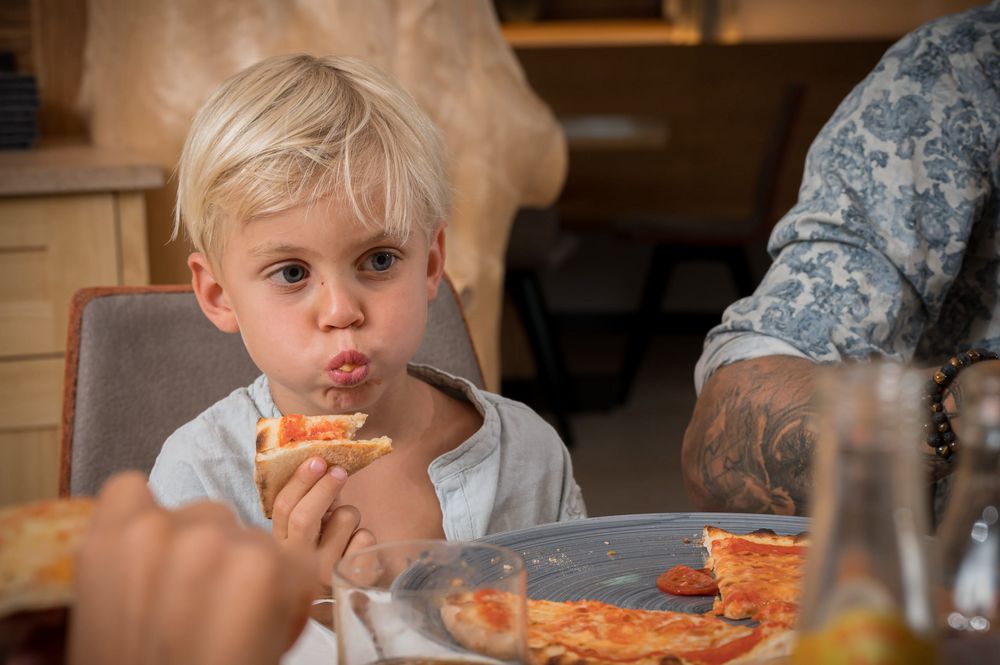 Kind mit blondem Haar isst Pizza am Tisch