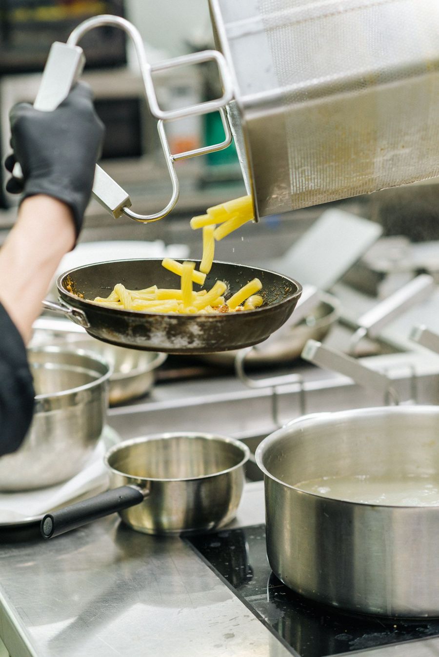 Hauskoch gießt gekochte Pasta in eine Pfanne in einer professionellen Küche.