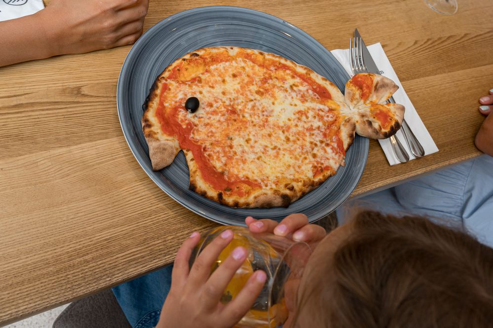Pizza in Fischform auf einem Teller, mit einer schwarzen Olive als Auge.