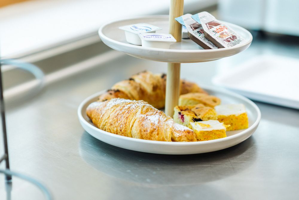 Zwei-stöckiges Tablett mit Croissants, kleinen Kuchenstücken und Nutella- sowie Butterportionen