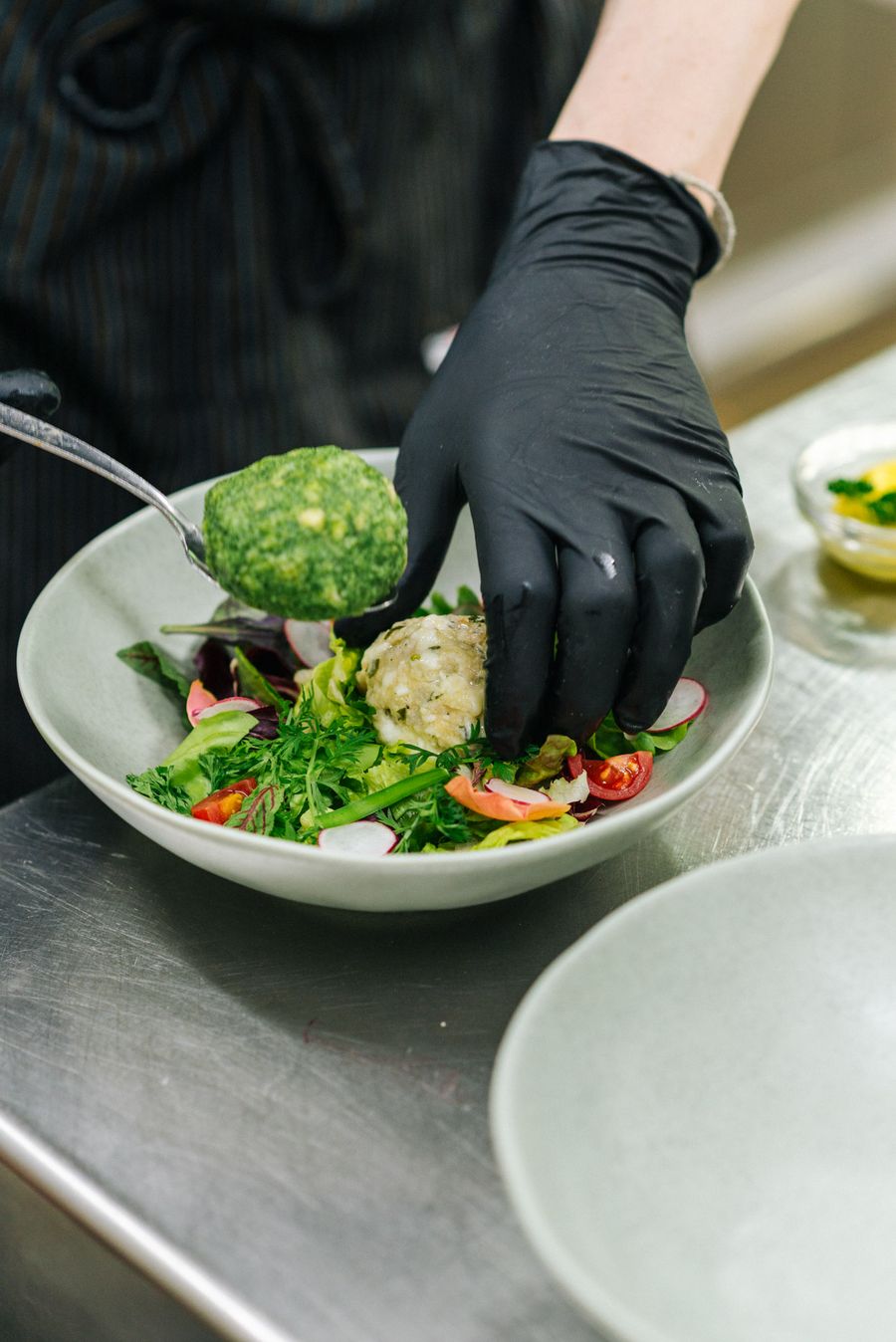 Koch mit schwarzer Handschuh legt Spinatknödel auf frischen Salat in Schüssel.