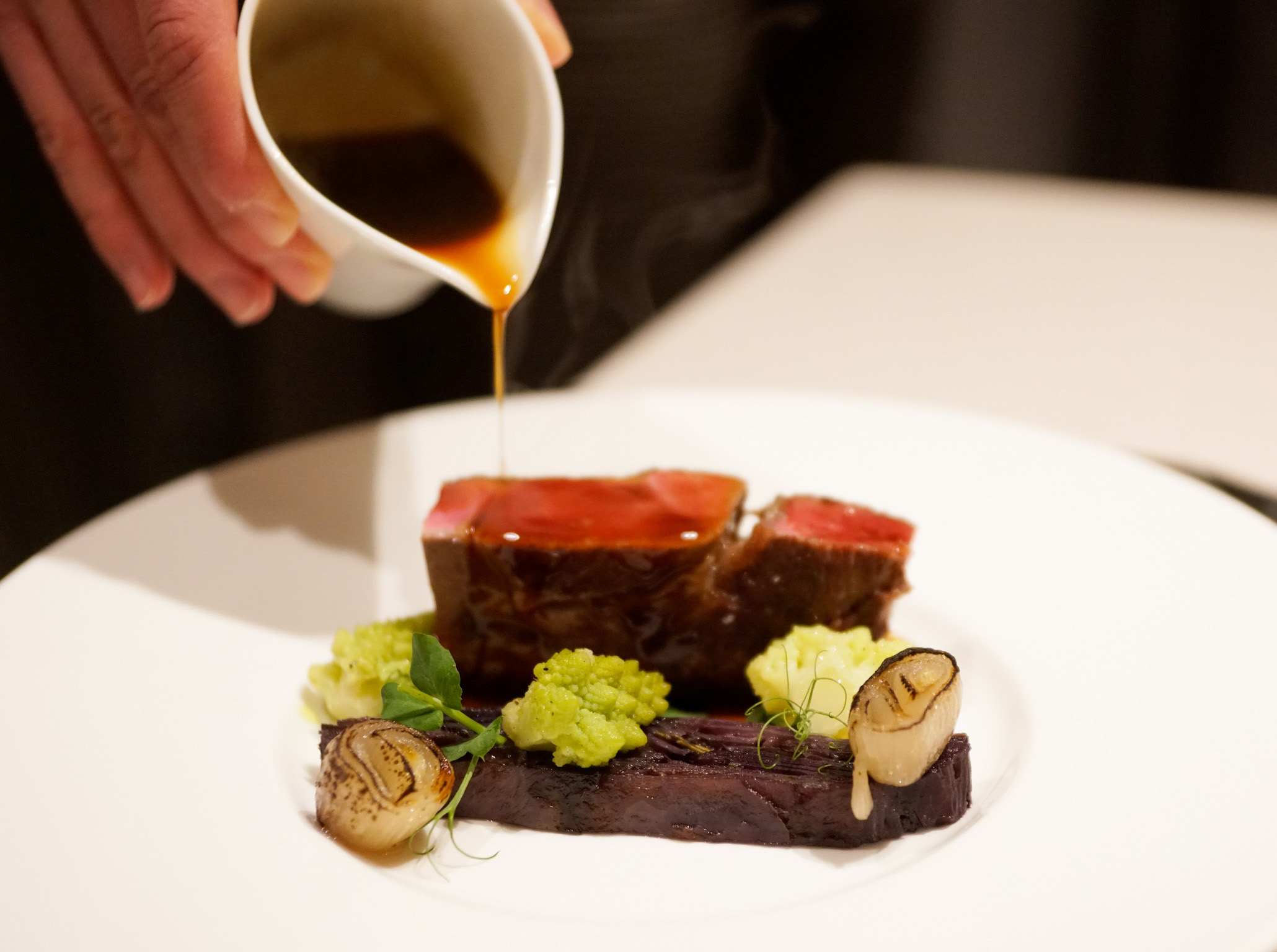 Fleischgericht mit Sauce, Gemüse und Zwiebeln auf weißem Teller.