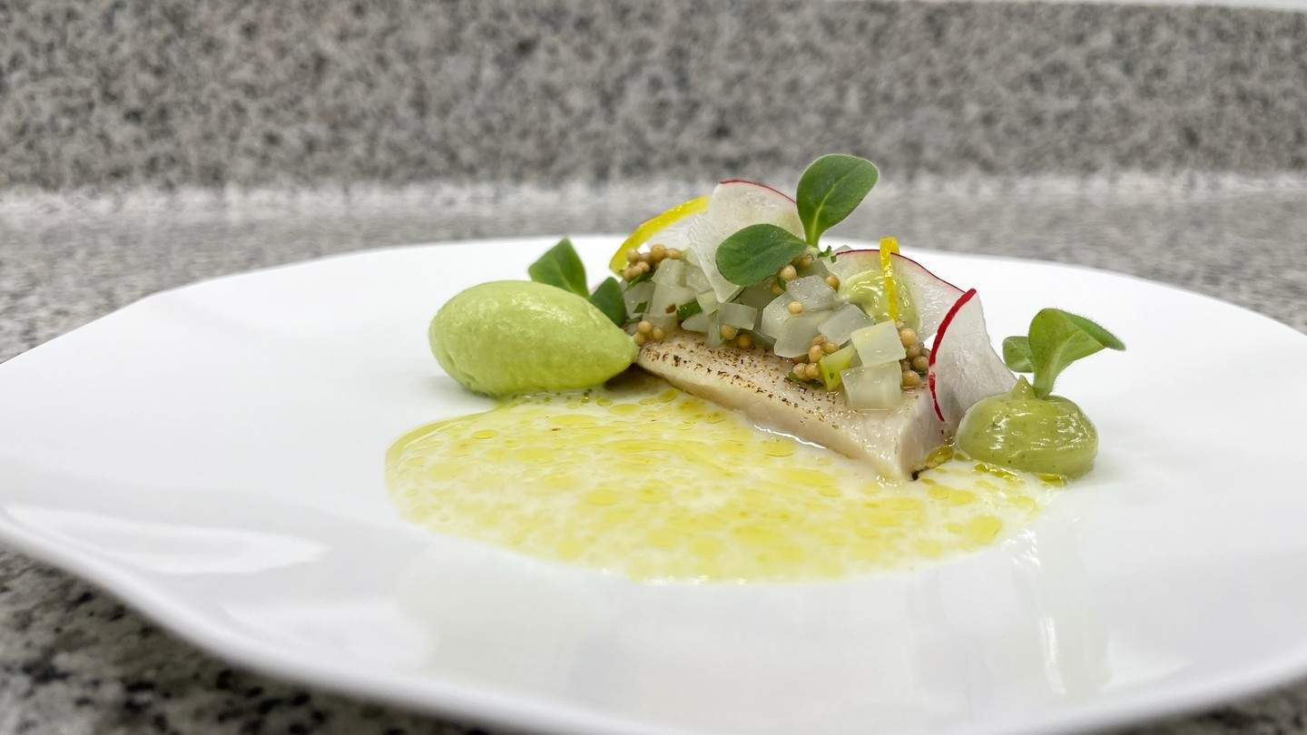 Fein angerichtetes Gericht mit Fisch, grüner Creme und Gemüsetopping auf weißem Teller